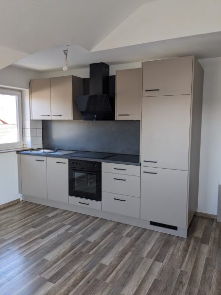 Helle Einbauküche Farbe Cappuccino mit grauen Fronten, schwarzer Dunstabzugshaube, Backofen und Kochfeld.