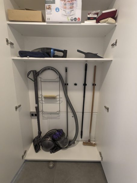 Putzschrank mit offenen Fächern zur Aufbewahrung von Staubsauger, Besen, Reinigungszubehör und Vorräten.