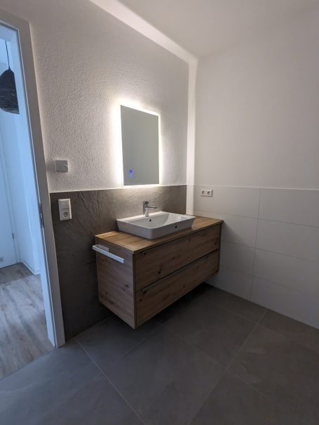 Modernes Bad mit schwebendem Holz-Waschtisch, eckigem Waschbecken und beleuchtetem Spiegel.