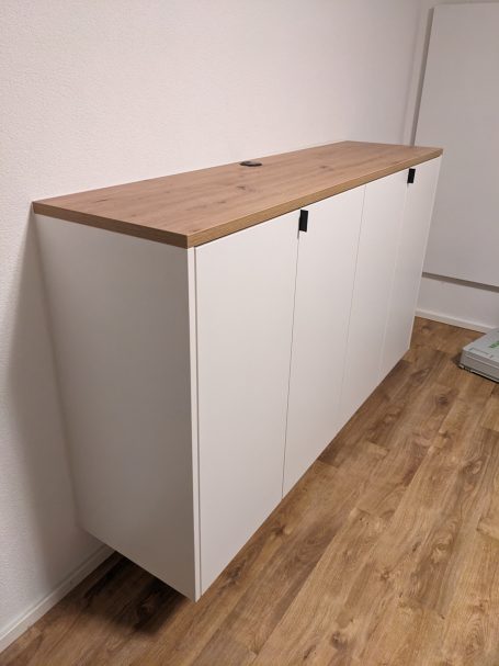 Schlichter Sideboard-Schrank mit weißer Front und Holzplatte auf hellem Boden.