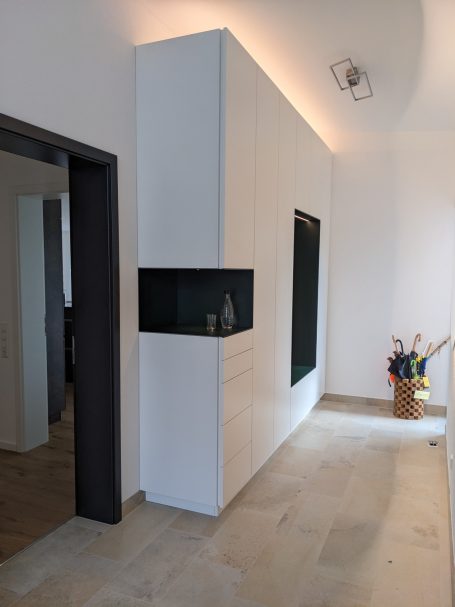 Moderner Eingangsbereich mit Einbauschrank in Weiß, integriertem schwarzen Wandfach und hellem Bodenbelag.