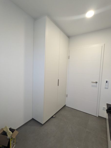 Büro mit hohem, weißen Einbauschrank und moderner weißer Tür in einem hellen Arbeitszimmer mit grauem Boden.
