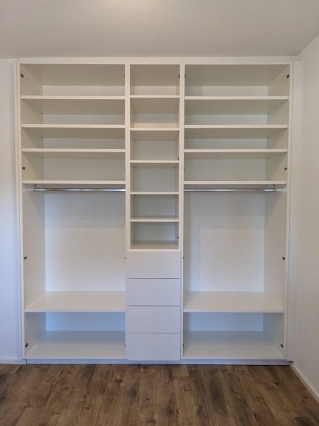 Offener Einbauschrank mit weißen Regalen, Kleiderstangen und Schubladen zur individuellen Aufbewahrung.