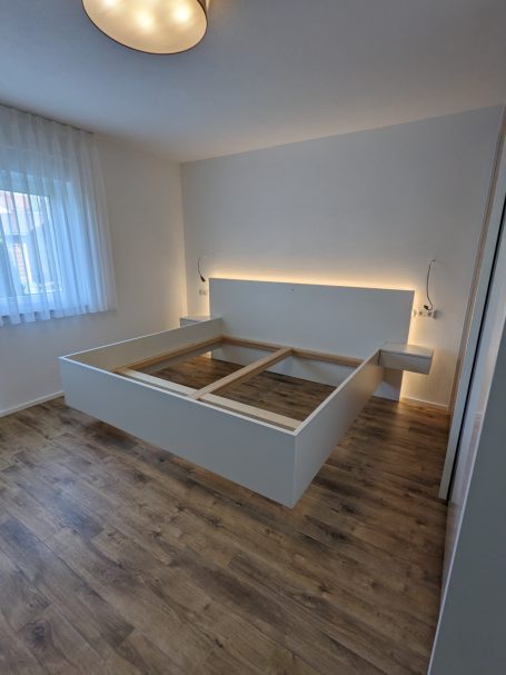 Modernes Bettgestell mit beleuchtetem Kopfteil und schwebenden Nachttischen in hellem Schlafzimmer.