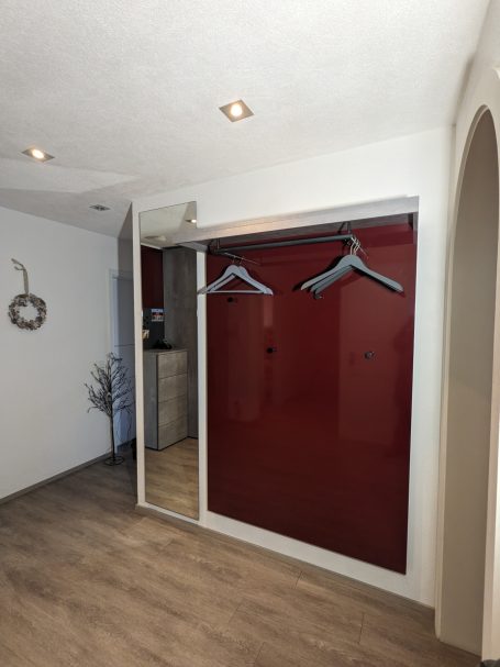 Garderobe mit großer roter Hochglanz-Wandverkleidung, Spiegel und Kleiderstange.