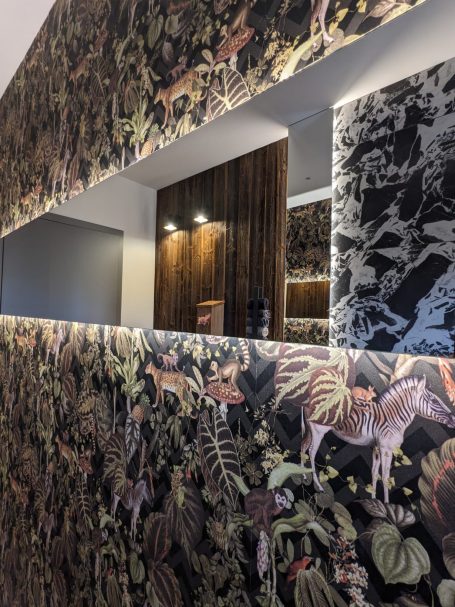 Badezimmer mit auffälliger gemusterter Tapete, großem Wandspiegel und indirekter Beleuchtung.