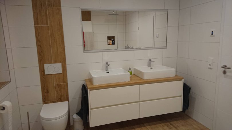 Zeitloses Badezimmer mit Doppelwaschtisch, zwei rechteckigen Becken auf Holzplatte und großem Spiegel.